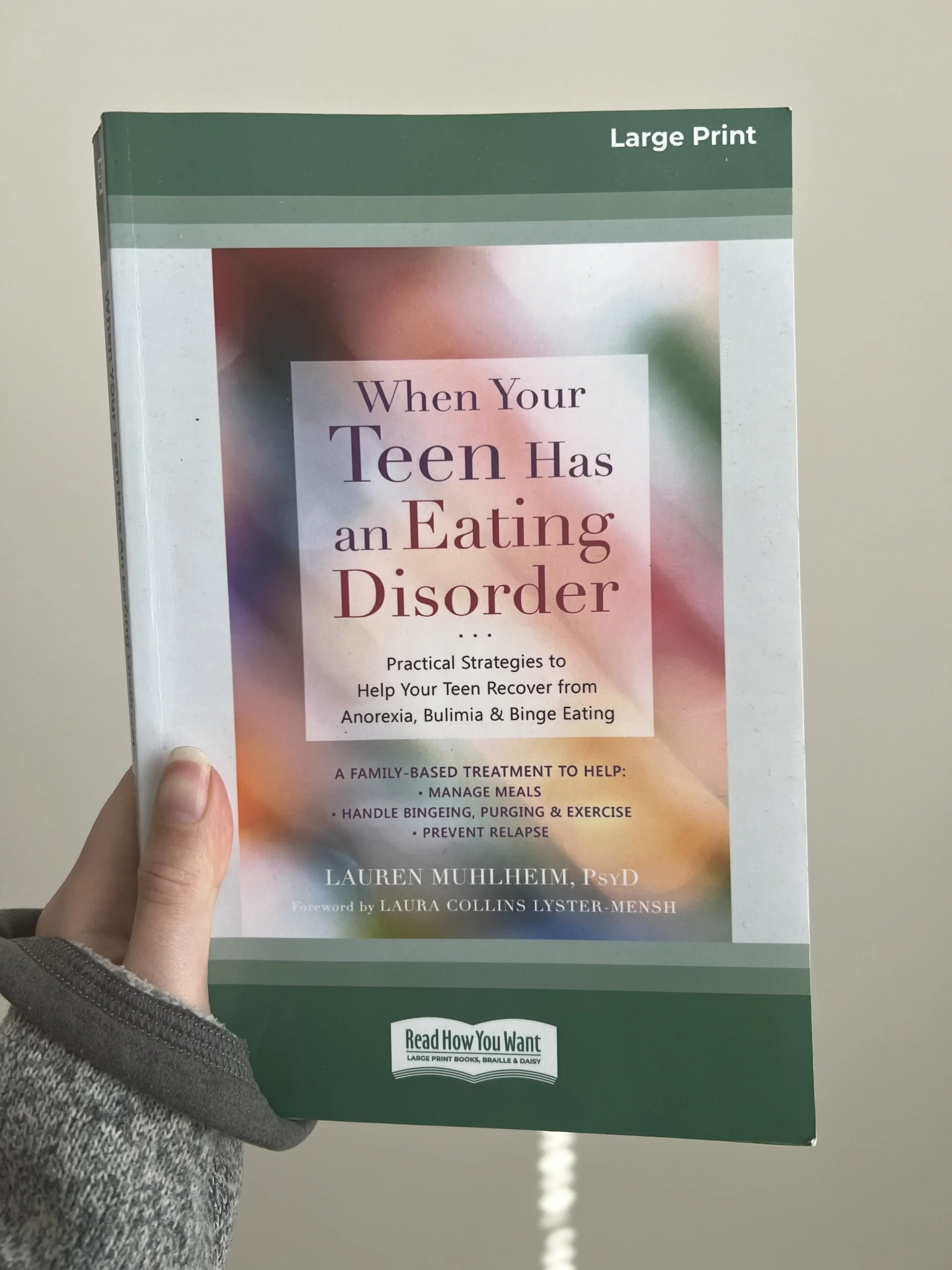  Alt Text: Photo of a hand holding the book “When Your Teen Has an Eating Disorder” by Dr. Lauren Muhlheim 